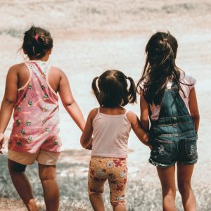 Helping-children-reach-their-full-potential-Three little girls from behind holding hands and walking in nature