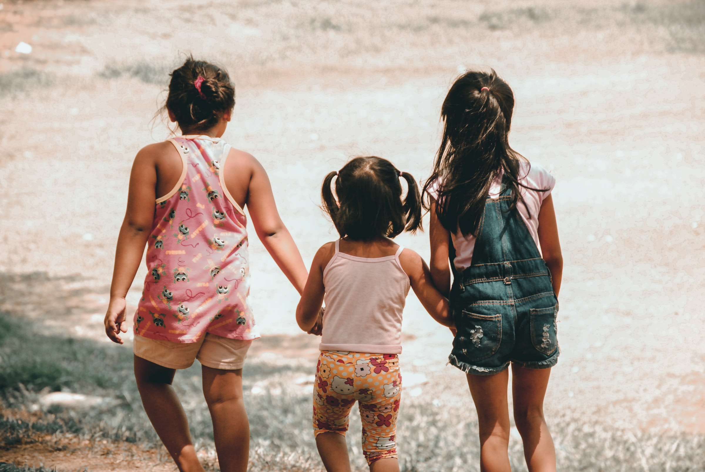 Helping-children-reach-their-full-potential-Three little girls from behind holding hands and walking in nature