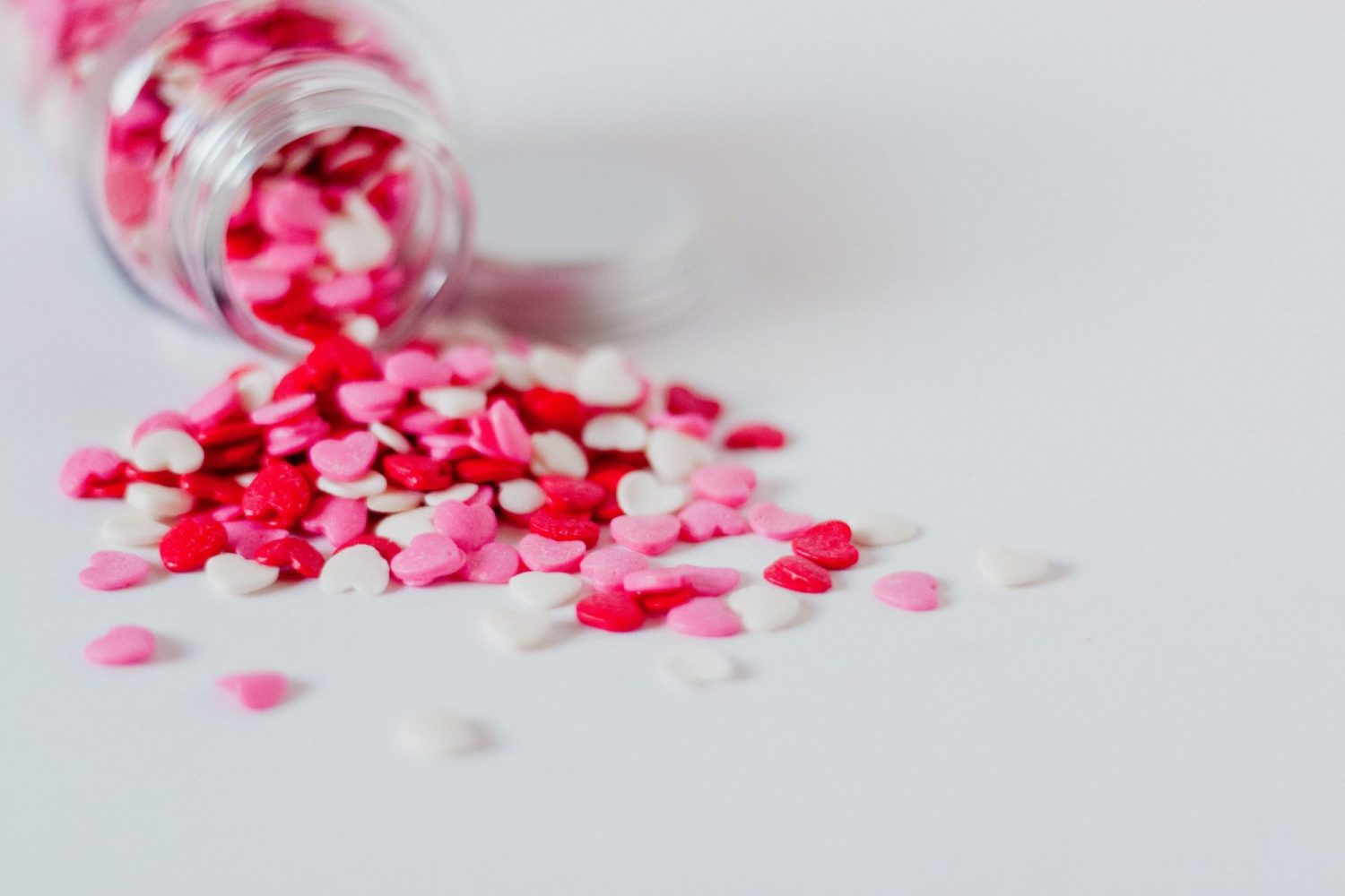 100 ways to show your children you love them-a jar placed one side down of red, pink and white hearts spilled