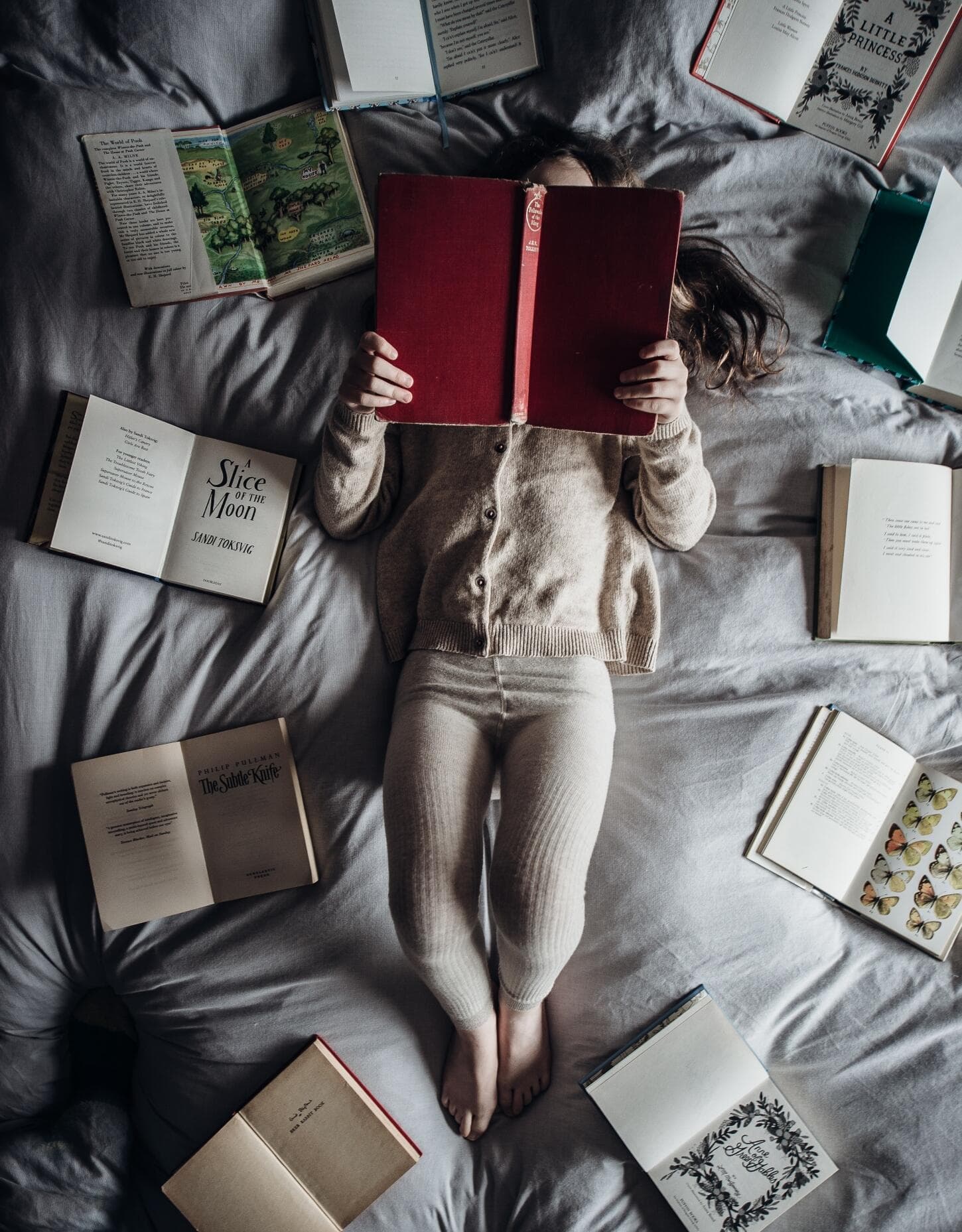 child guidance for parents JoannaBel-little girl lying on the bed surrounded by books and holding one at the head level covering her head